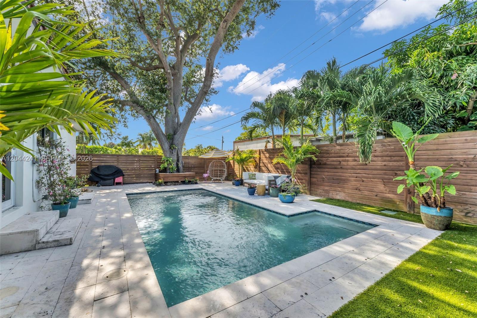 A backyard features a rectangular swimming pool, stone patio, wooden fencing, and a large tree — 2220 SW 25th St, Miami FL 33133, MIAMI, FL