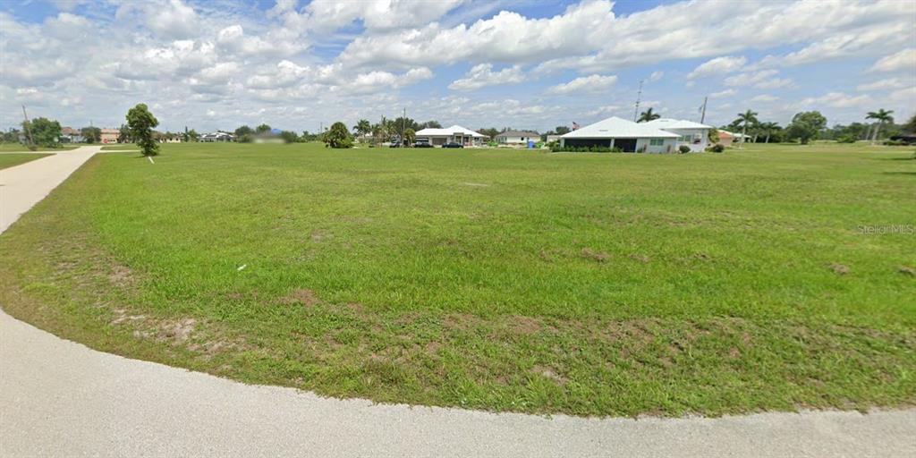 A large, grassy vacant lot is situated along a paved road in a residential area — 17336 OPHIR LANE, PUNTA GORDA, FL