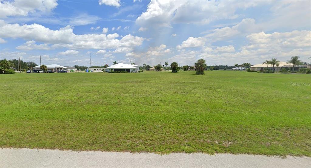 A wide, grassy vacant lot sits under a blue sky with scattered white clouds — 17336 OPHIR LANE, PUNTA GORDA, FL