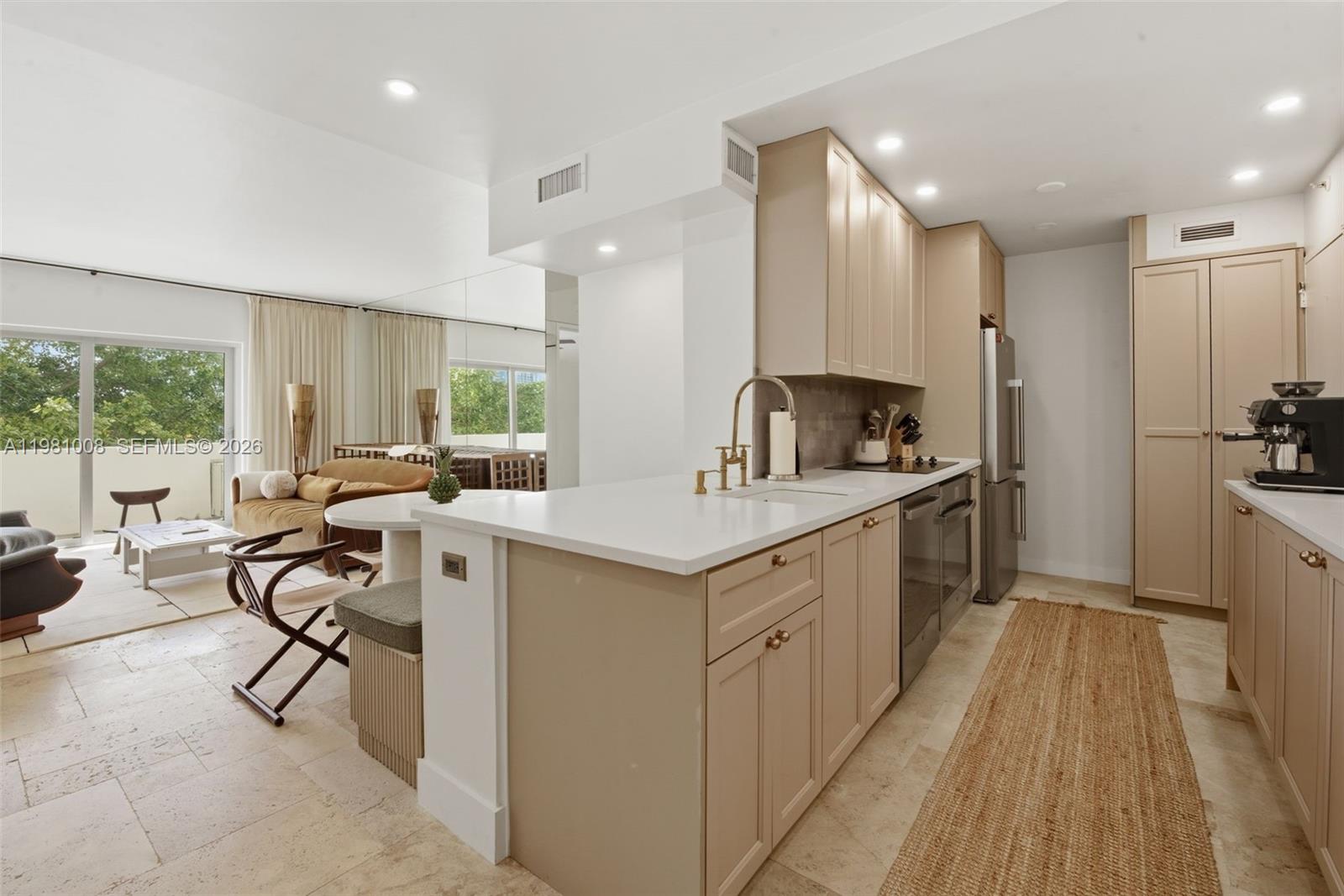 A kitchen with beige cabinets and white countertops opens into a living area with balcony access — 3 Island Ave # 06K, Miami Beach FL 33139, MIAMI BEACH, FL