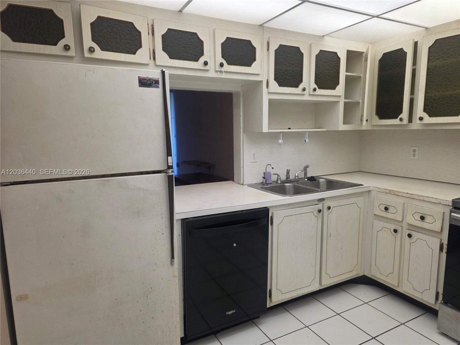 A kitchen features white cabinets with dark inserts, a black dishwasher, and white tile flooring — 1304 NE 191st St # 128, Miami FL 33179, MIAMI, FL