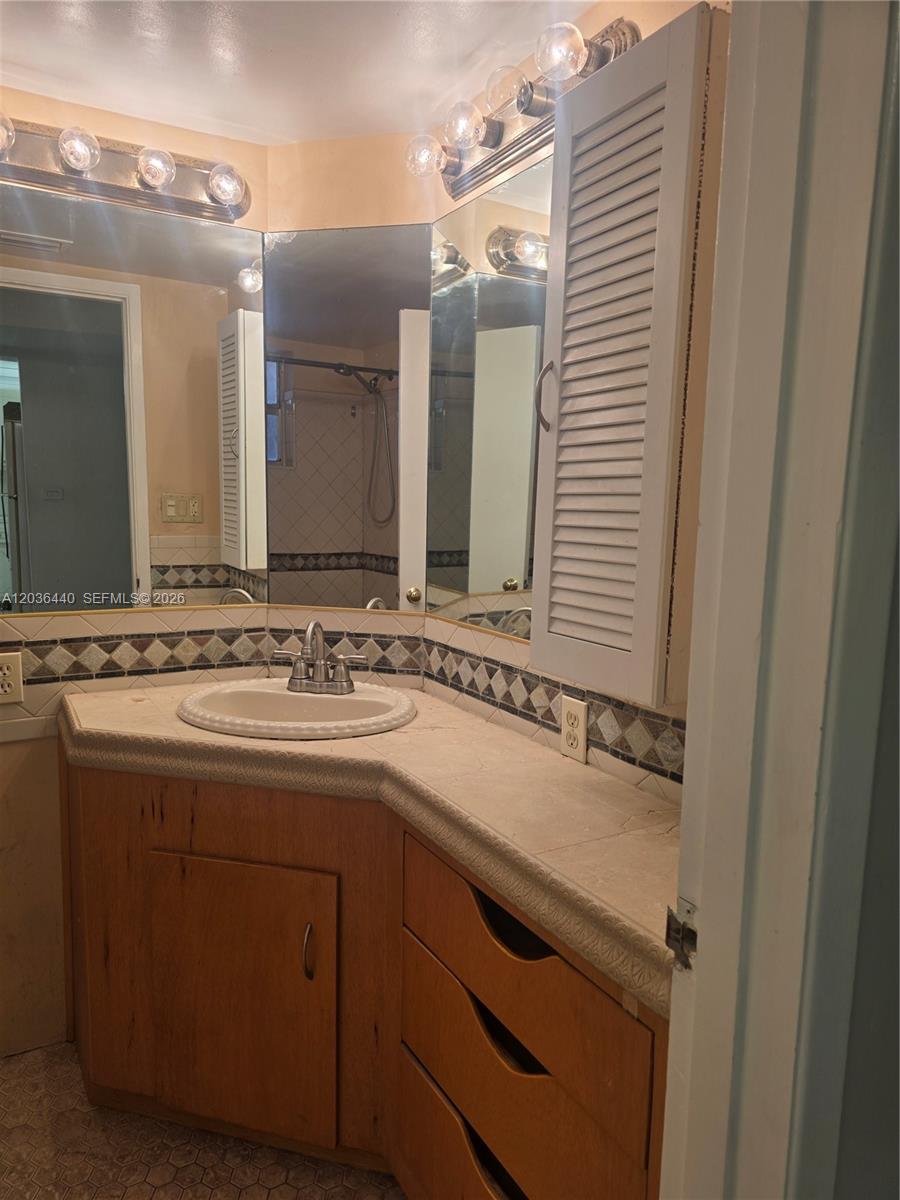 A bathroom features a corner vanity with a tiled countertop, wood cabinetry, and a mirror — 1304 NE 191st St # 128, Miami FL 33179, MIAMI, FL