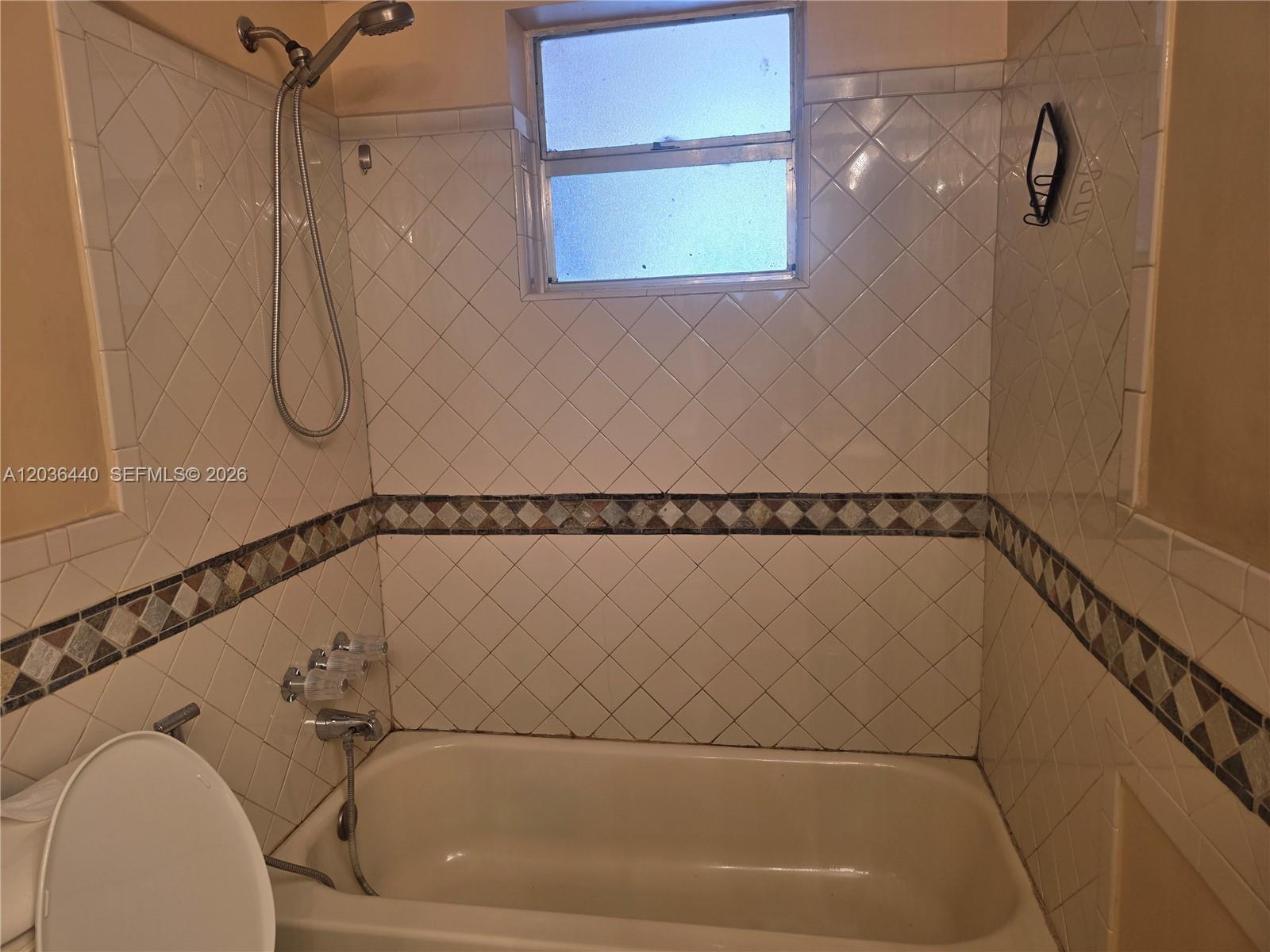 A bathroom features a bathtub with a shower head and diamond-patterned wall tiles — 1304 NE 191st St # 128, Miami FL 33179, MIAMI, FL
