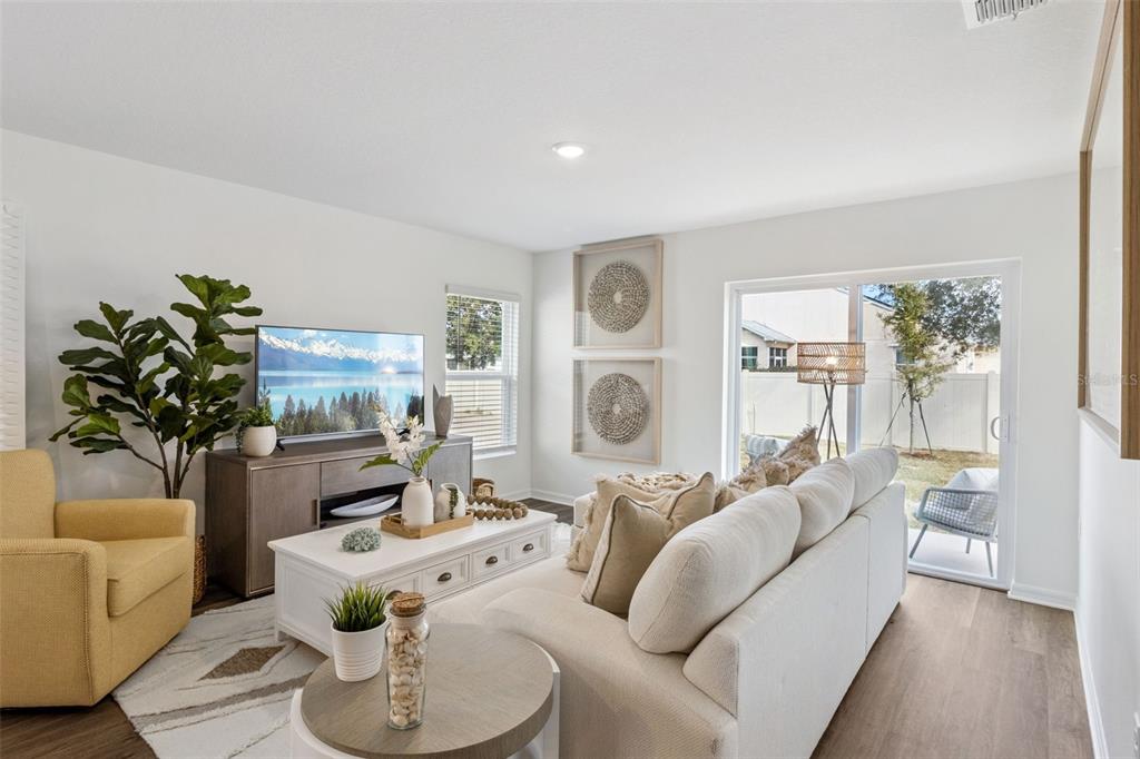 A bright living room features a beige sofa, yellow armchair, coffee table, and sliding glass doors — 761 GREENWAY BOULEVARD, LAKE WALES, FL