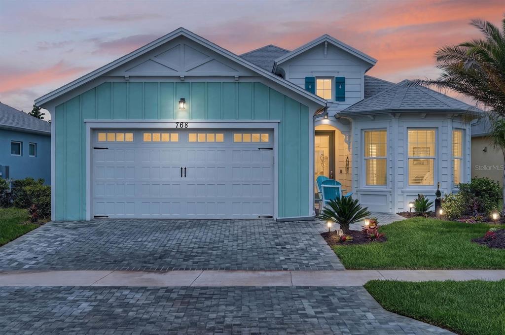 A single-story house with a turquoise garage, white trim, and a paver driveway at dusk — 768 MARGARITAVILLE AVENUE, DAYTONA BEACH, FL