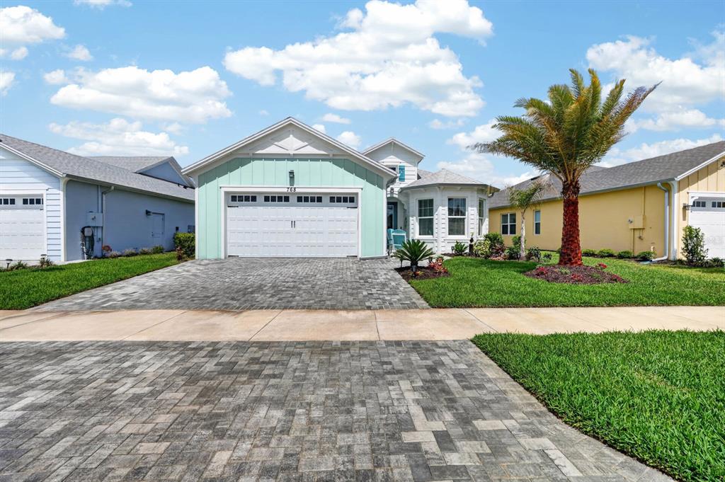A light green house with a two-car garage and a paved driveway under a blue sky — 768 MARGARITAVILLE AVENUE, DAYTONA BEACH, FL