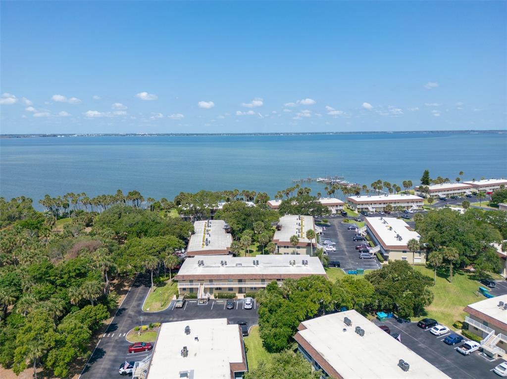 An aerial view shows multi-story apartment buildings surrounded by trees near a large body of water — 6500 FALCON WAY UNIT 19D, CAPE CANAVERAL, FL