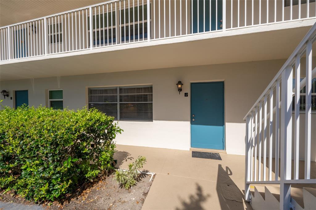 The exterior of a multi-story building features a blue door, white railings, and landscaping — 6500 FALCON WAY UNIT 19D, CAPE CANAVERAL, FL