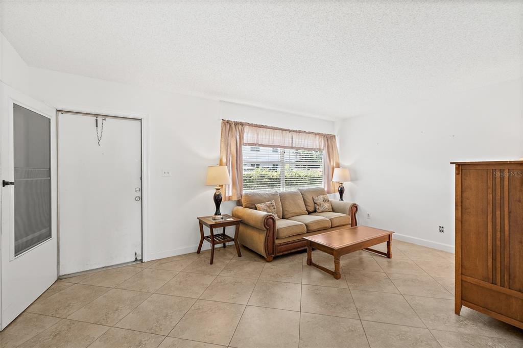 A living room with beige tile flooring, a tan sofa, a coffee table, and a window — 6500 FALCON WAY UNIT 19D, CAPE CANAVERAL, FL
