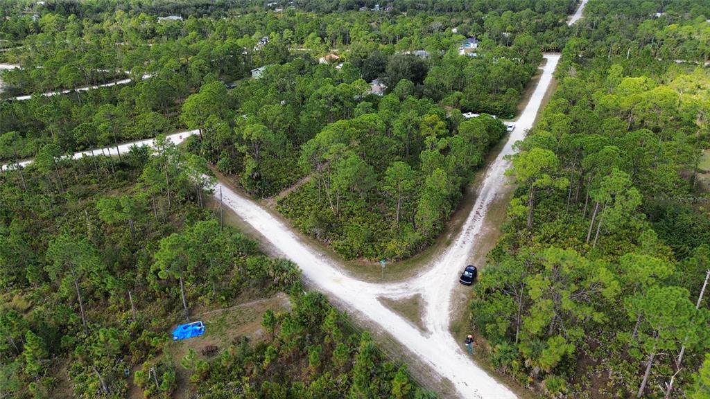 An aerial view shows a dirt road intersection surrounded by dense trees and vegetation — 13343 MENDERES DRIVE, PUNTA GORDA, FL