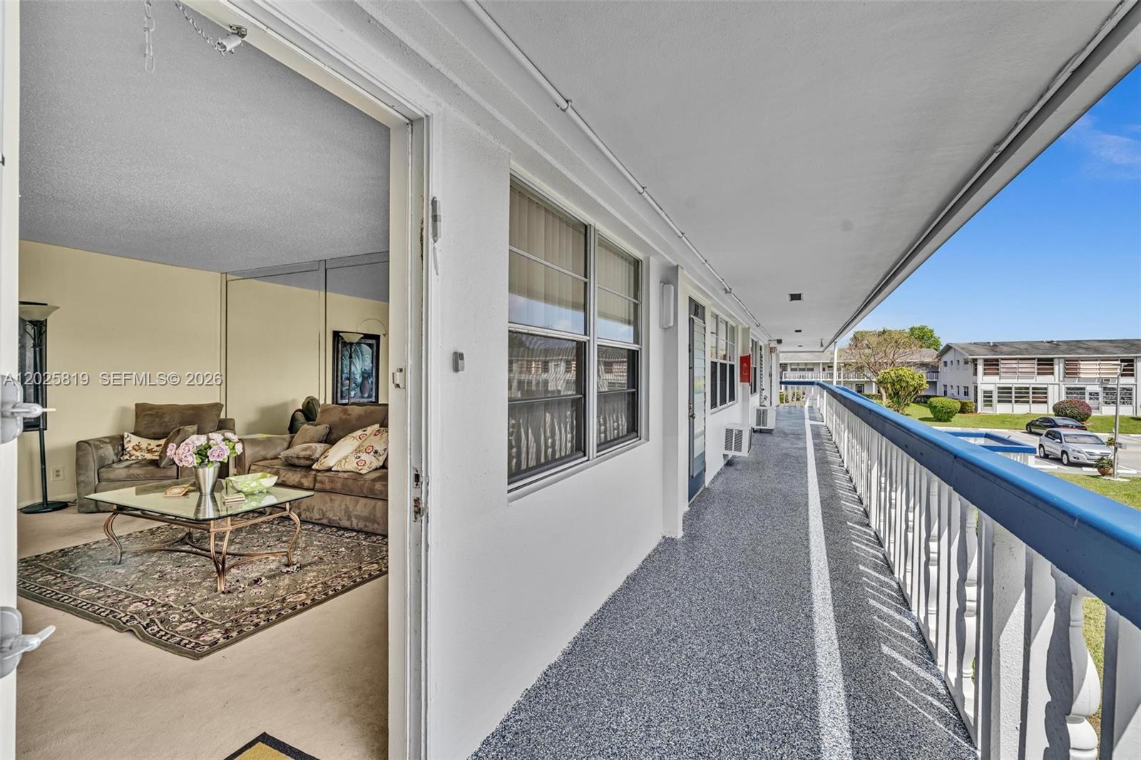 A view from a balcony looking into a living room with a glass coffee table — 117 Westbury  E # 117, Deerfield Beach FL 33442, DEERFIELD BEACH, FL