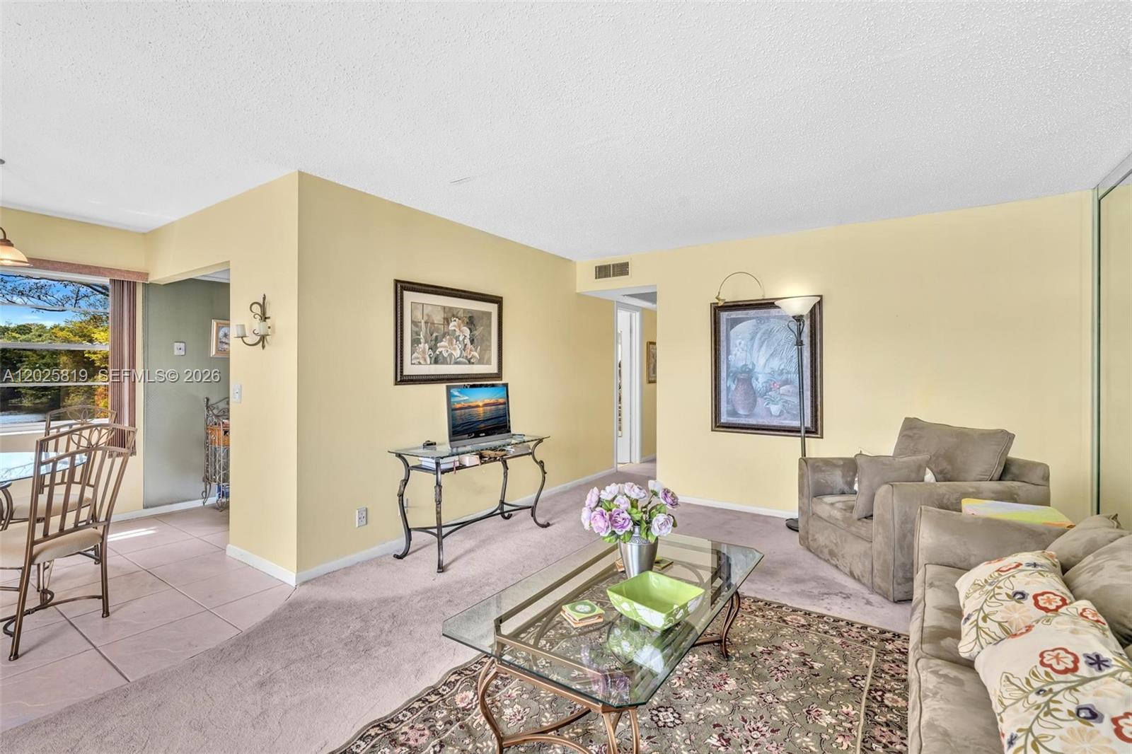 A living room features yellow walls, beige carpeting, a glass coffee table, and a sofa — 117 Westbury  E # 117, Deerfield Beach FL 33442, DEERFIELD BEACH, FL