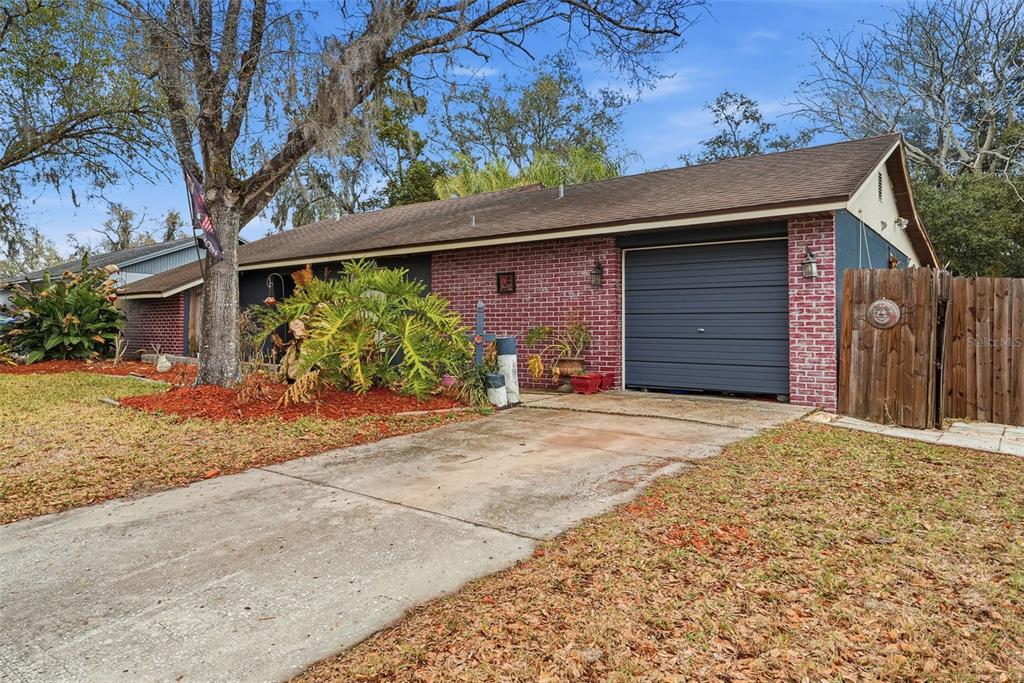 A single-story brick house with a dark garage door and a concrete driveway — 17603 CRANBROOK DRIVE, LUTZ, FL