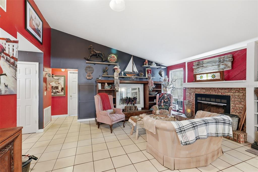 A living room features a brick fireplace, tiled floors, and a dark accent wall with shelving — 17603 CRANBROOK DRIVE, LUTZ, FL
