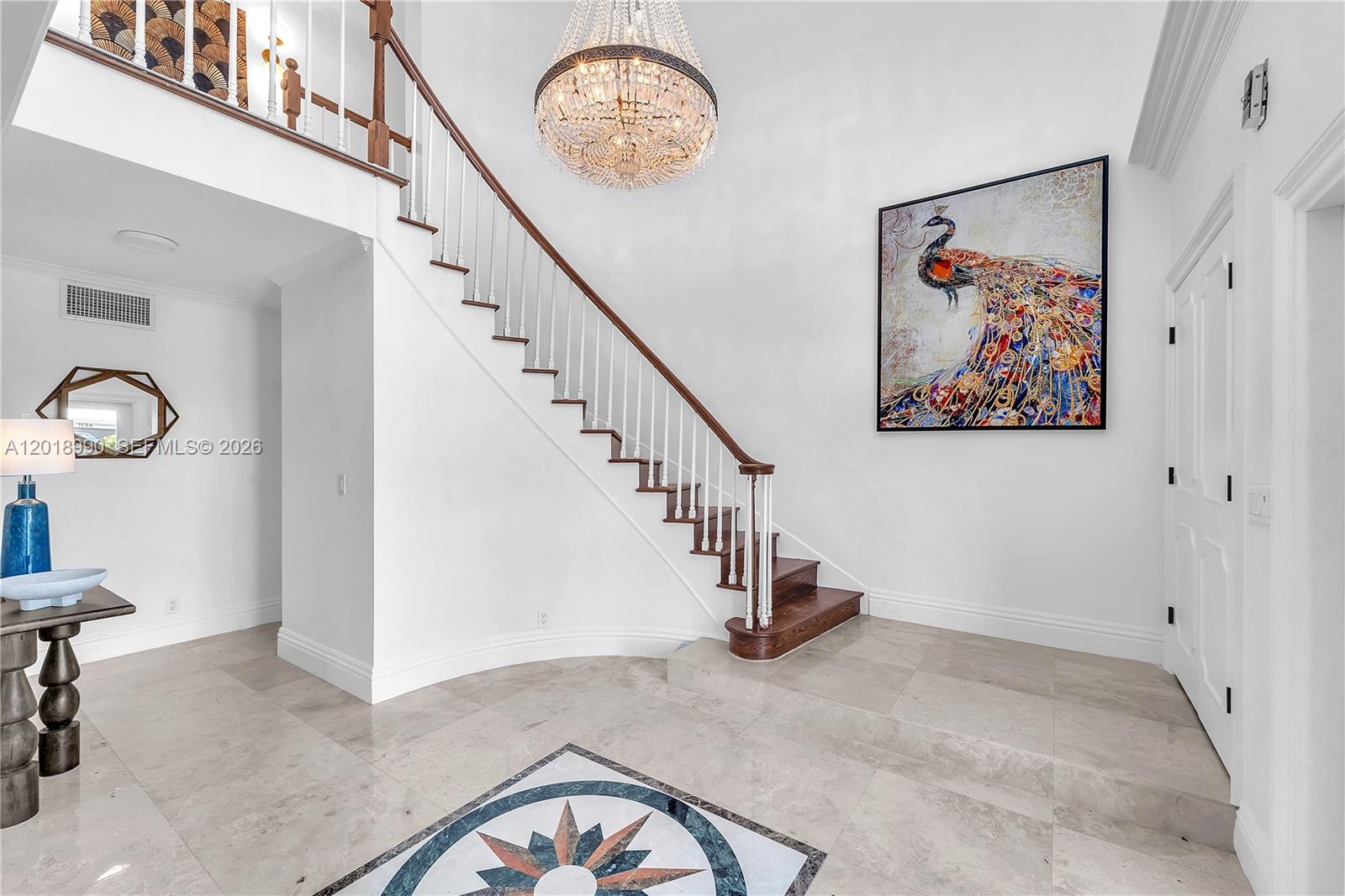 A grand foyer features a crystal chandelier, a staircase with wooden railings, and tiled flooring — 4440 NE 23rd Ave, Lighthouse Point FL 33064, LIGHTHOUSE POINT, FL
