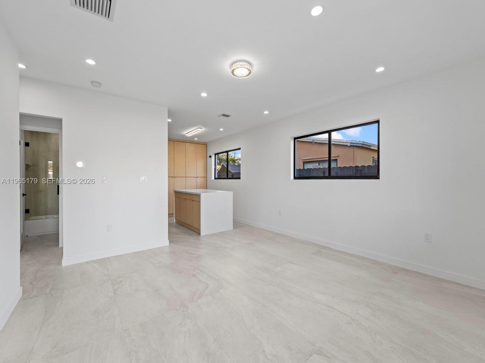 A bright, minimalist room features light tile flooring, recessed lighting, and a small kitchen area — 3620 SW 92nd Ave, Miami FL 33165, MIAMI, FL