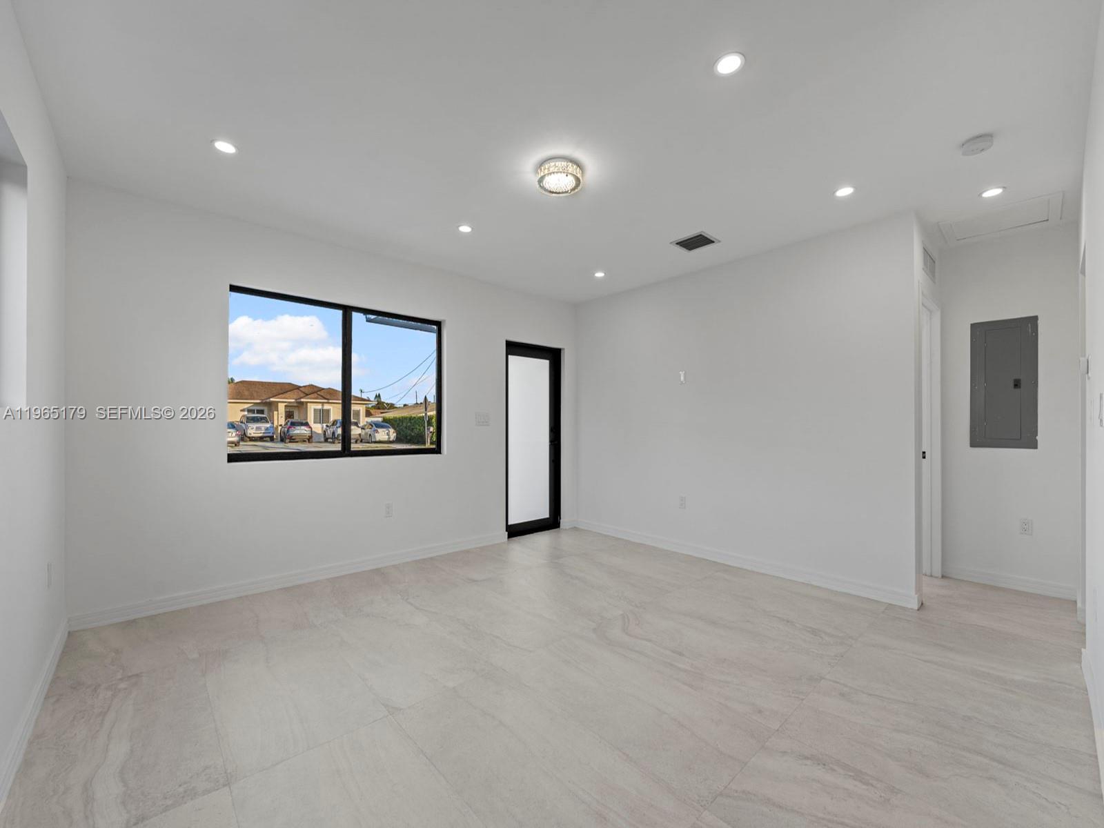 A bright, empty room features white walls, large light-colored floor tiles, and a black-framed window — 3620 SW 92nd Ave, Miami FL 33165, MIAMI, FL