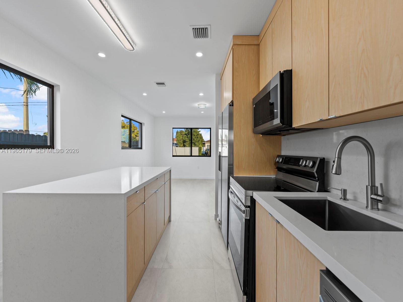 A modern kitchen features light wood cabinetry, white quartz countertops, and stainless steel appliances — 3620 SW 92nd Ave, Miami FL 33165, MIAMI, FL