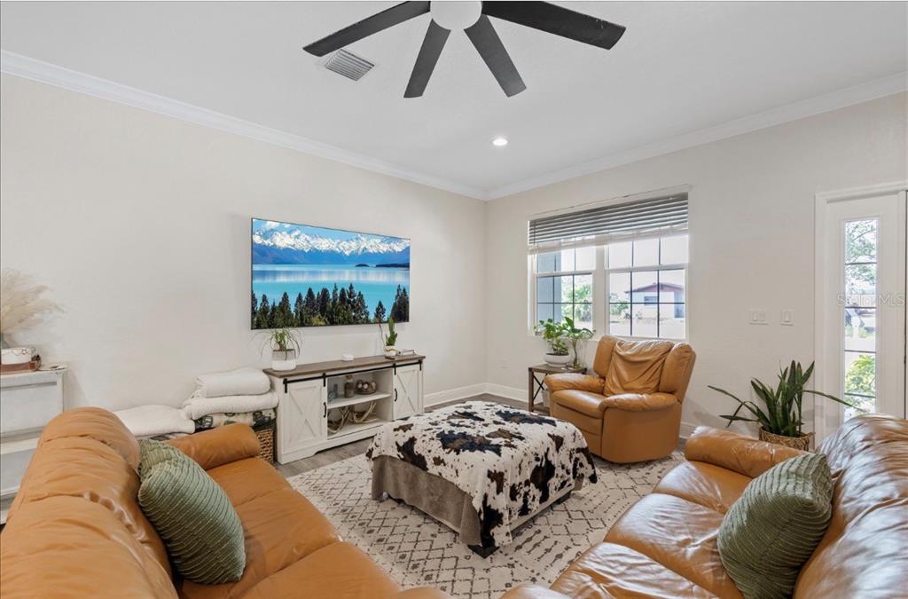 A living room features tan leather sofas, a cowhide ottoman, and a wall-mounted television — 1311 W WASHINGTON STREET UNIT A, PLANT CITY, FL