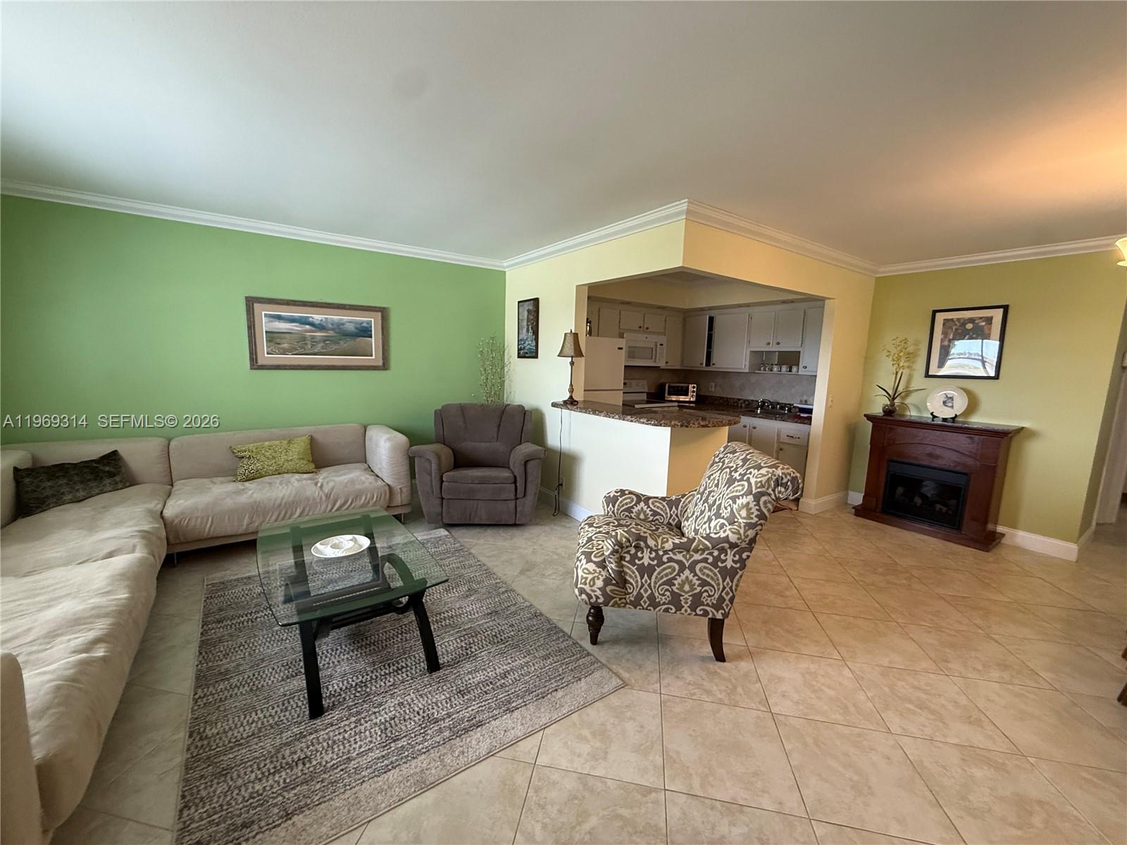 A living room features a sectional sofa, patterned armchair, glass coffee table, and fireplace — 127 Tuscany B # 127, Delray Beach FL 33446, DELRAY BEACH, FL