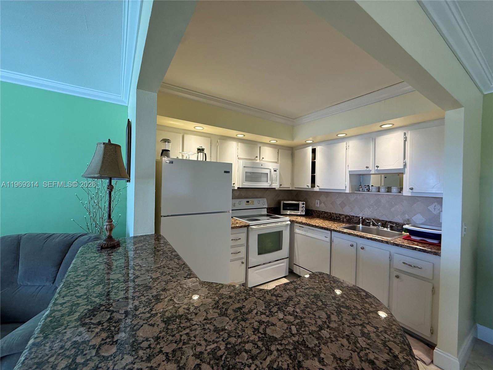 A kitchen features white cabinets, granite countertops, and white appliances under recessed lighting — 127 Tuscany B # 127, Delray Beach FL 33446, DELRAY BEACH, FL