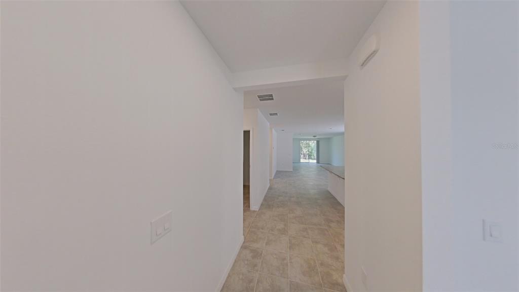 A view down a tiled hallway leading into an open-concept living area with large windows — 2404 WHITE TAIL STREET, DAVENPORT, FL