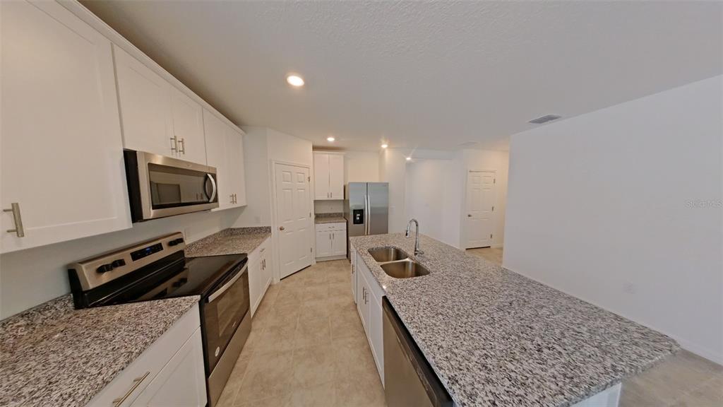 A modern kitchen features white cabinets, granite countertops, stainless steel appliances, and a central island — 2404 WHITE TAIL STREET, DAVENPORT, FL
