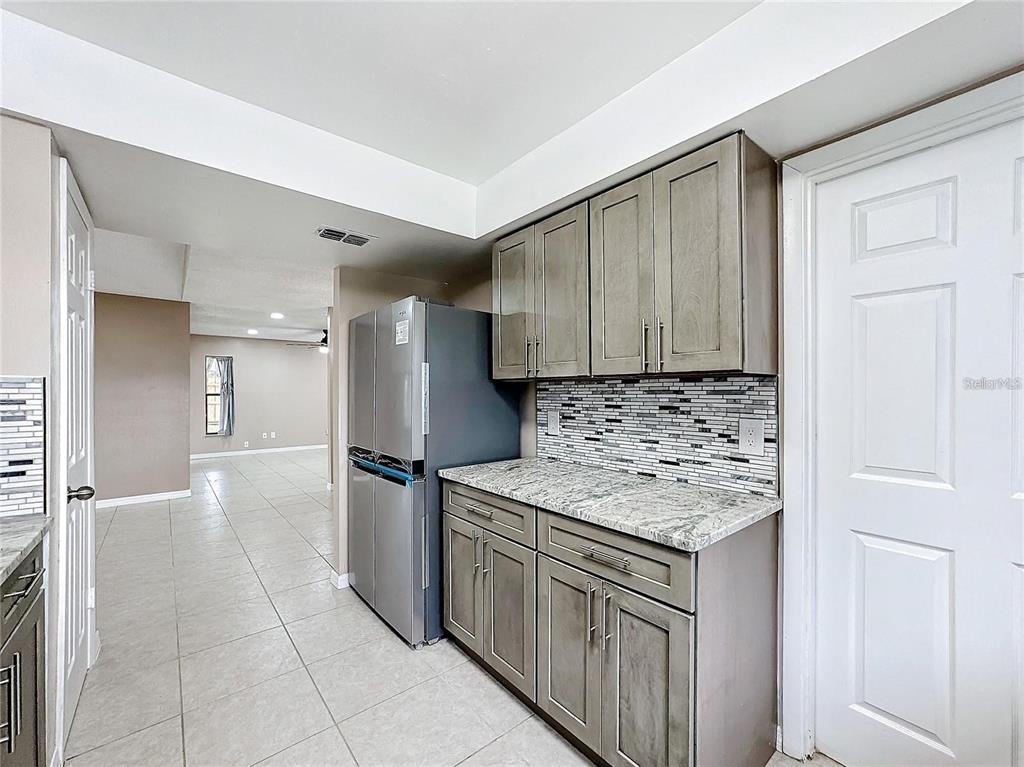A kitchen area features grey cabinets, a stainless steel refrigerator, and a tiled backsplash — 103 ALAMEDA DRIVE, KISSIMMEE, FL