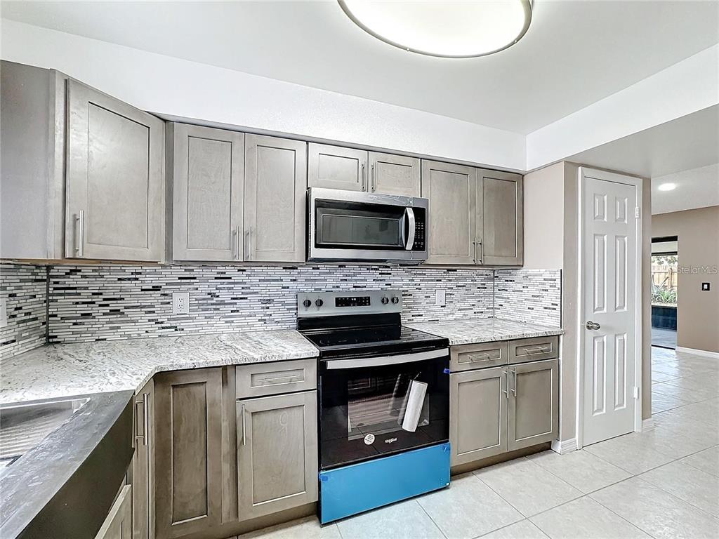A kitchen features gray shaker cabinets, granite countertops, a tiled backsplash, and stainless steel appliances — 103 ALAMEDA DRIVE, KISSIMMEE, FL