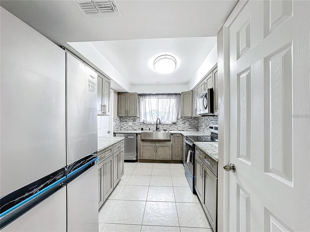A galley kitchen features gray cabinets, stainless steel appliances, a farmhouse sink, and tile flooring — 103 ALAMEDA DRIVE, KISSIMMEE, FL