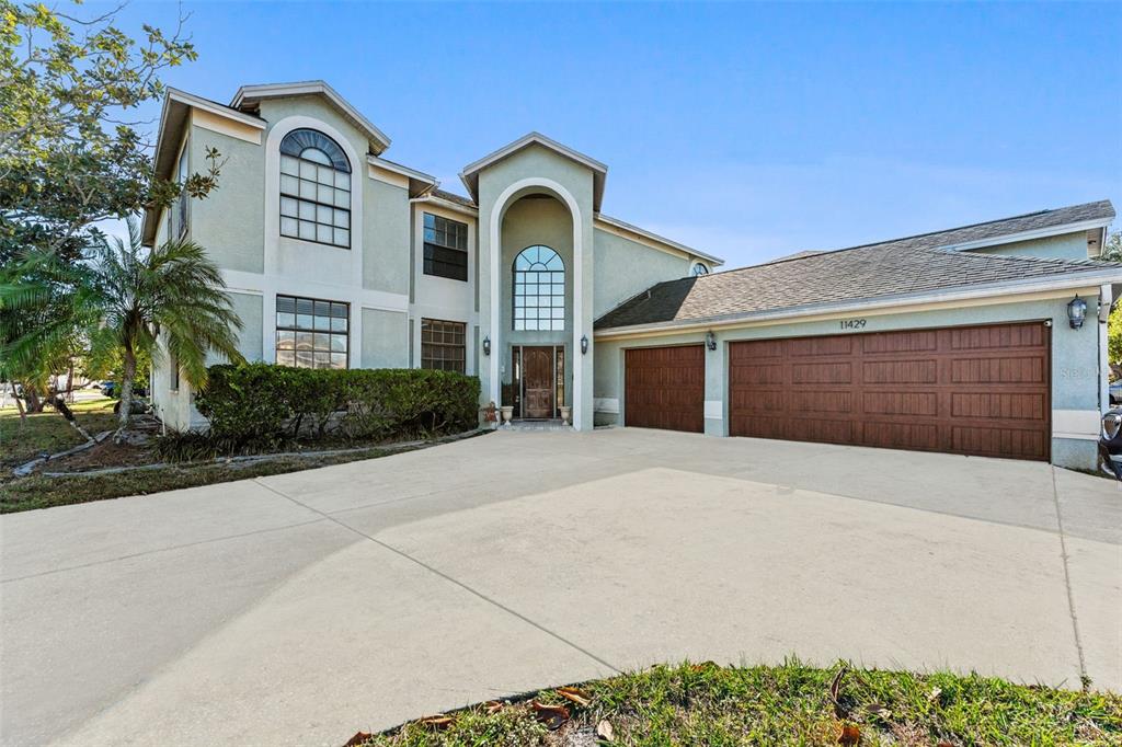 A two-story house with a light-colored stucco exterior, arched entryway, and a three-car garage — 11429 ZENITH CIRCLE, TAMPA, FL