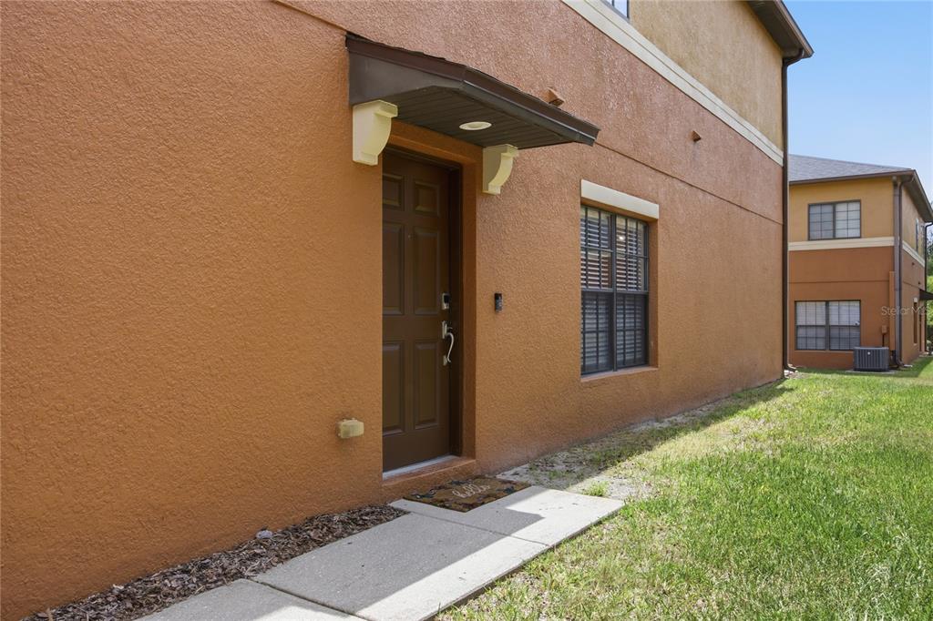 A side view of a tan stucco building with a brown door and window — 1033 BLACKWATER DRIVE, WESLEY CHAPEL, FL