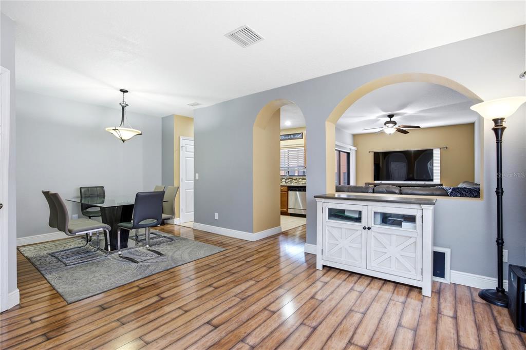 A dining area with a glass table and rug opens into a living room with arches — 1033 BLACKWATER DRIVE, WESLEY CHAPEL, FL