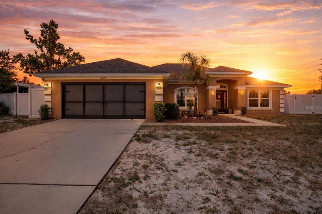 A single-story house with a tan stucco exterior, dark garage door, and a sunset sky — 14061 WHITE PLAINS STREET, SPRING HILL, FL