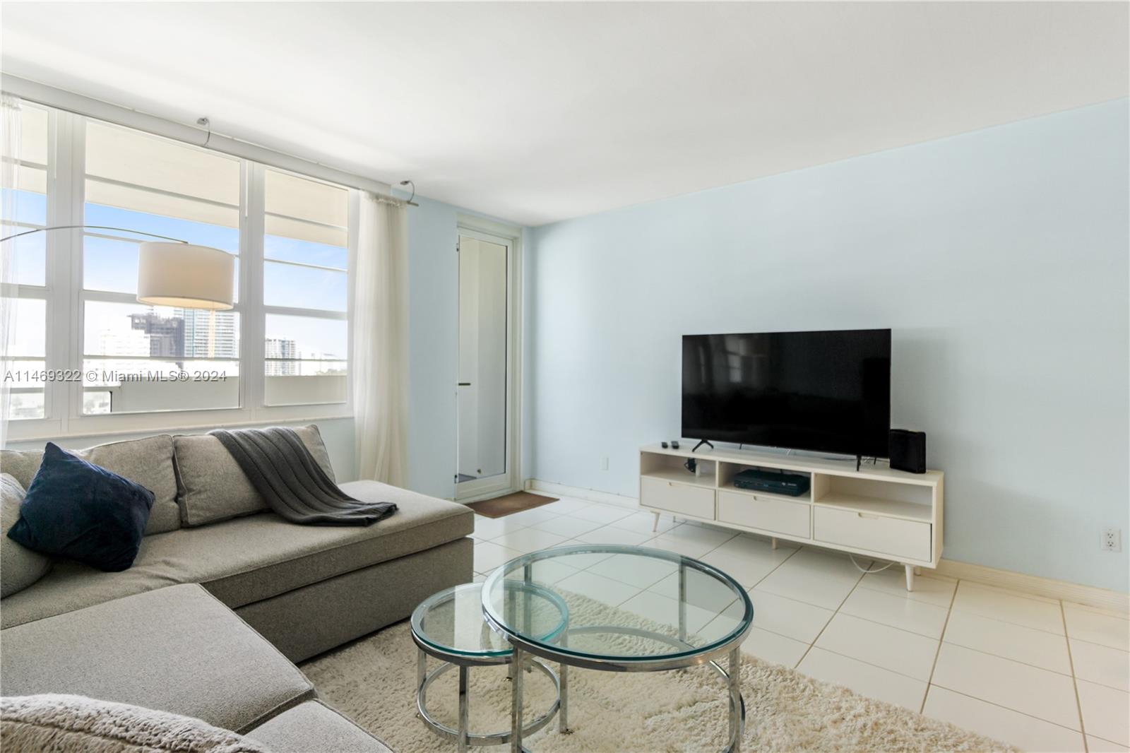 A living room features a grey sectional sofa, glass coffee tables, and a television console — 100 Lincoln Rd # 1043, Miami Beach FL 33139, MIAMI BEACH, FL