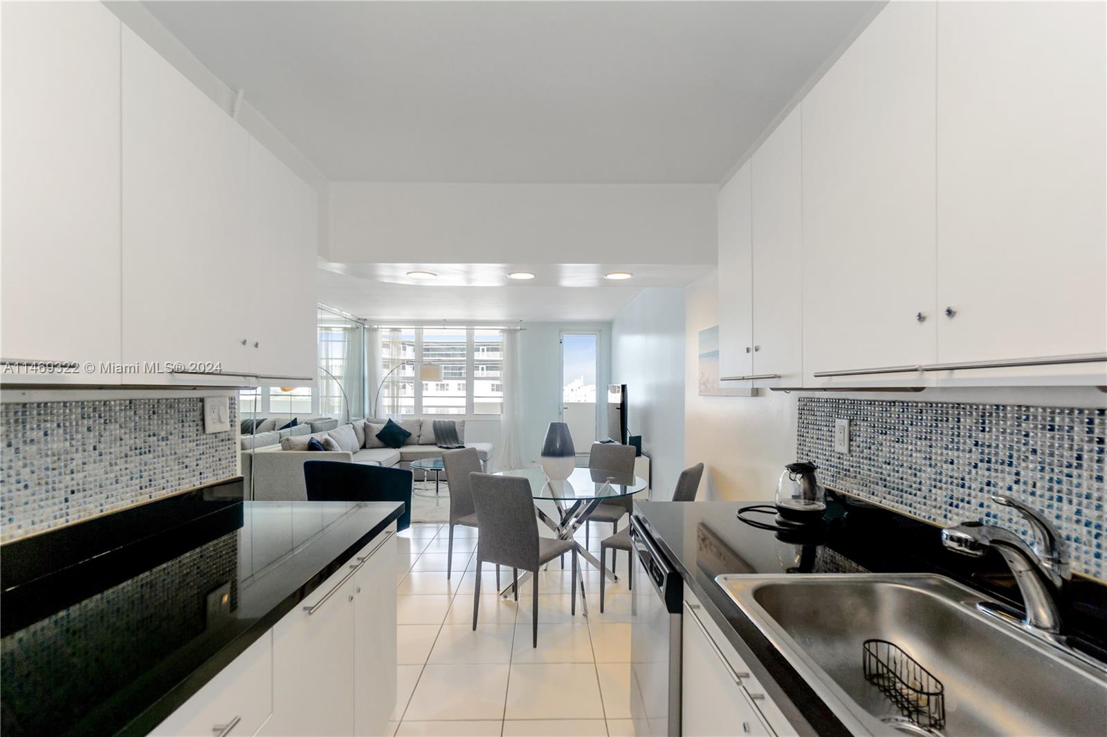 A kitchen with black countertops and white cabinets opens into a dining and living area — 100 Lincoln Rd # 1043, Miami Beach FL 33139, MIAMI BEACH, FL