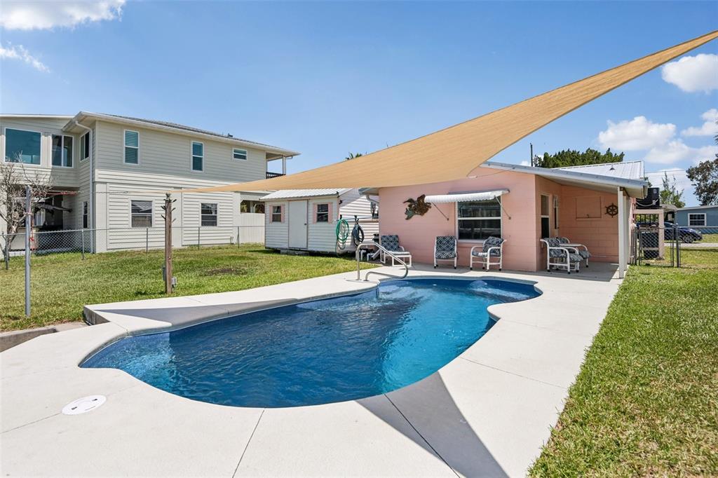 A backyard features a swimming pool, a pink house with a shade sail, and lawn — 3303 MINNOW CREEK DRIVE, HERNANDO BEACH, FL