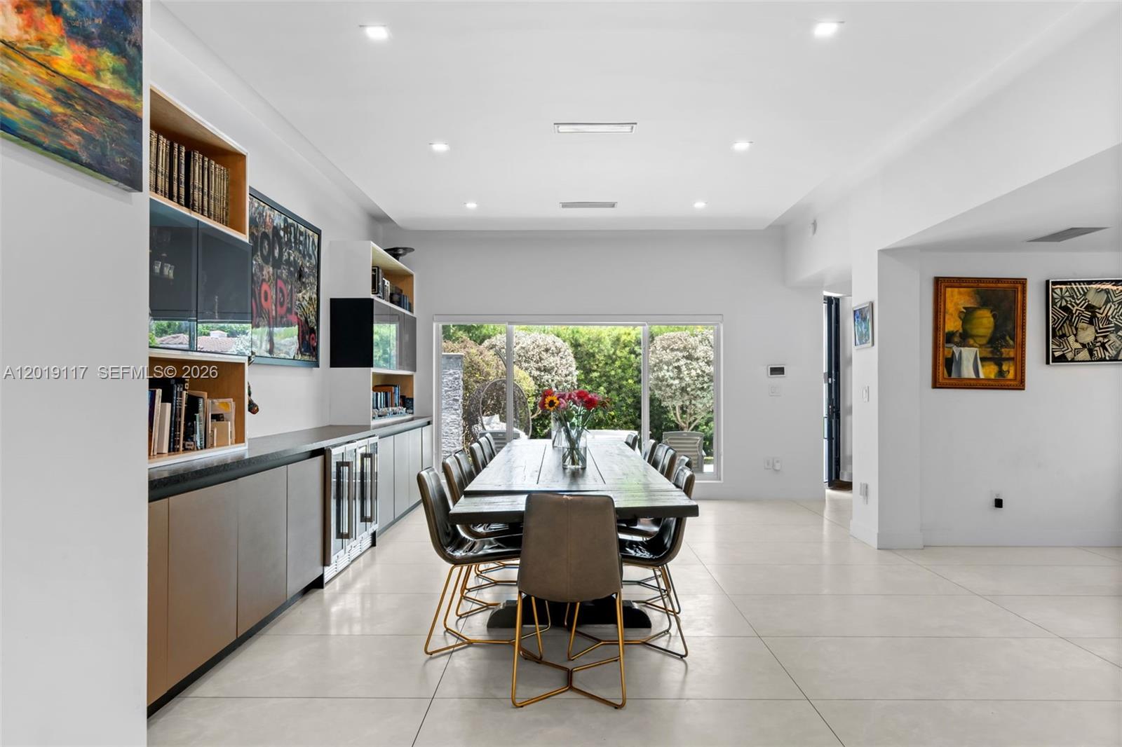A modern dining room features a long wooden table, built-in cabinetry, and large glass doors — 3748 Prairie Ave, Miami Beach FL 33140, MIAMI BEACH, FL