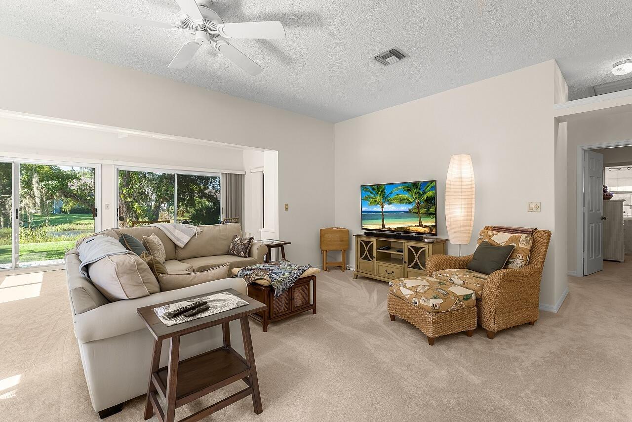 A living room features a beige sofa, wicker armchair with ottoman, television, and sliding glass doors — 431 Tamarind Place, Vero Beach FL 32962, VERO BEACH, FL