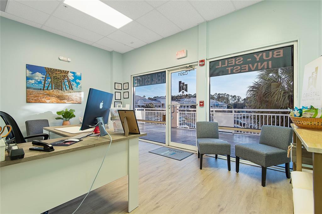 A real estate office features a desk, computer, two gray chairs, and a glass door — 160 CYPRESS POINT PARKWAY UNIT C201 A, PALM COAST, FL