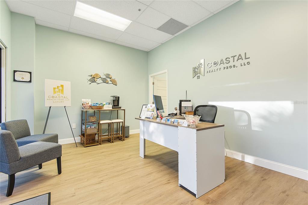 A reception area features a desk, two chairs, and Coastal Realty Pros branding on the wall — 160 CYPRESS POINT PARKWAY UNIT C201 A, PALM COAST, FL