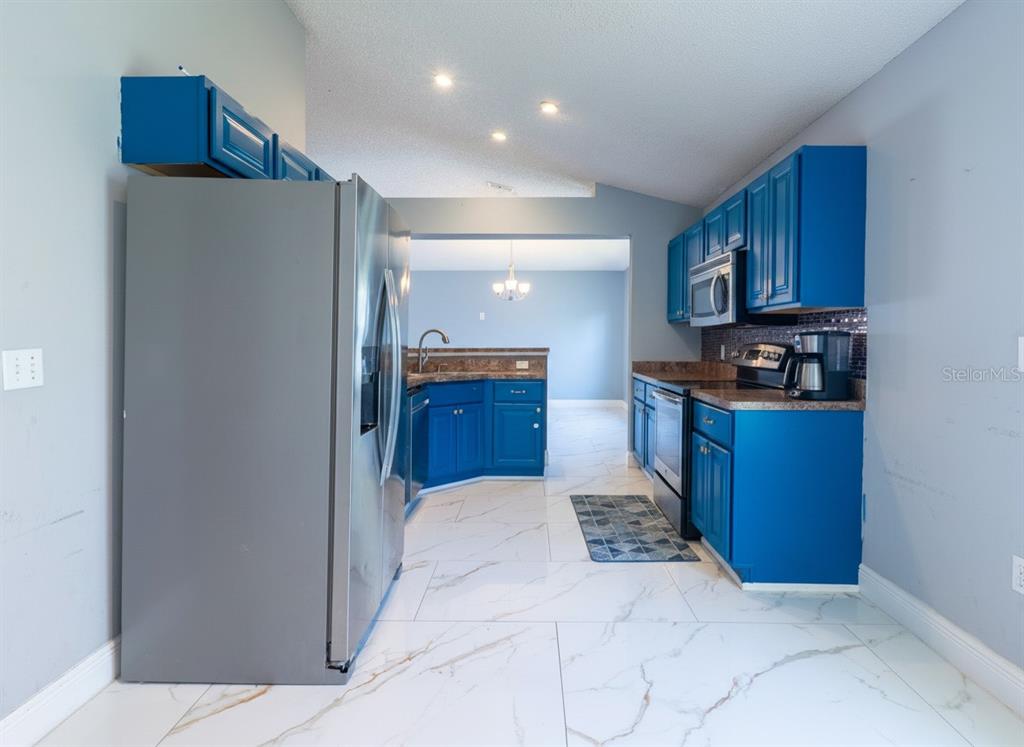 A kitchen features blue cabinets, stainless steel appliances, and white marble-patterned tile flooring — 12919 KINGS LAKE DRIVE, GIBSONTON, FL