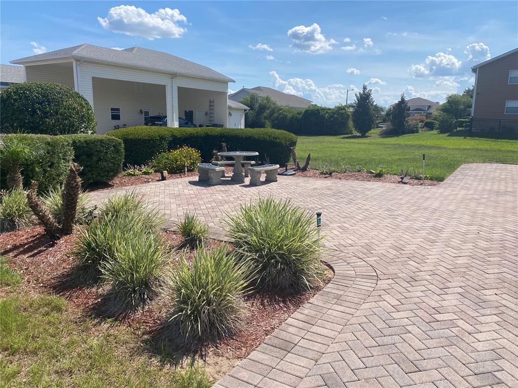 A paved patio features a stone table and bench set surrounded by landscaping and lawn — 368 MOTORCOACH DRIVE S, POLK CITY, FL