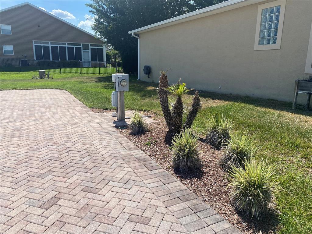 A paved driveway leads to a house exterior with a utility meter and small plants — 368 MOTORCOACH DRIVE S, POLK CITY, FL
