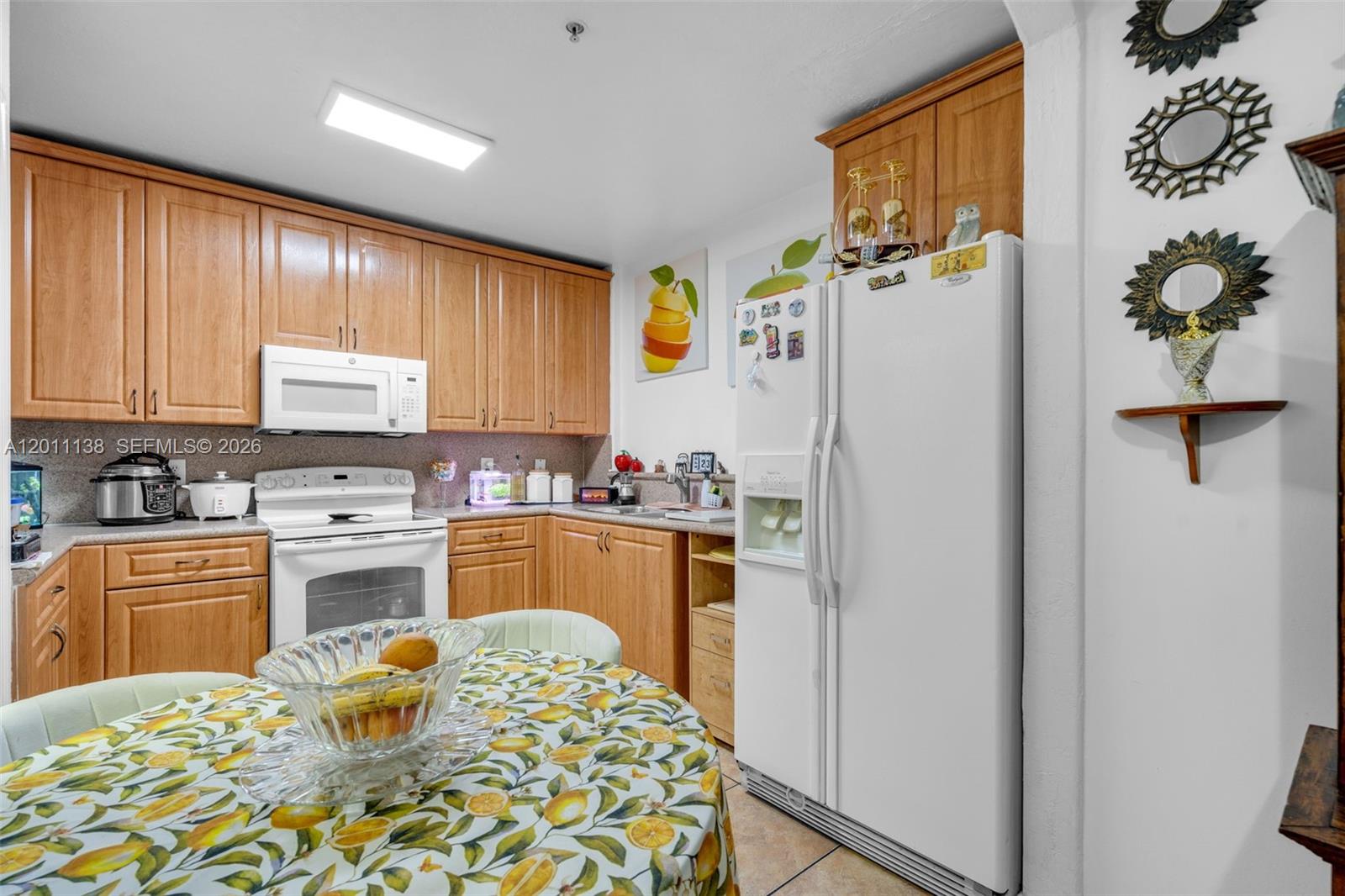 A kitchen features light wood cabinets, white appliances, and a round table with lemon-patterned cloth — 8031 W 36th Ave # 1, Hialeah FL 33018, HIALEAH, FL