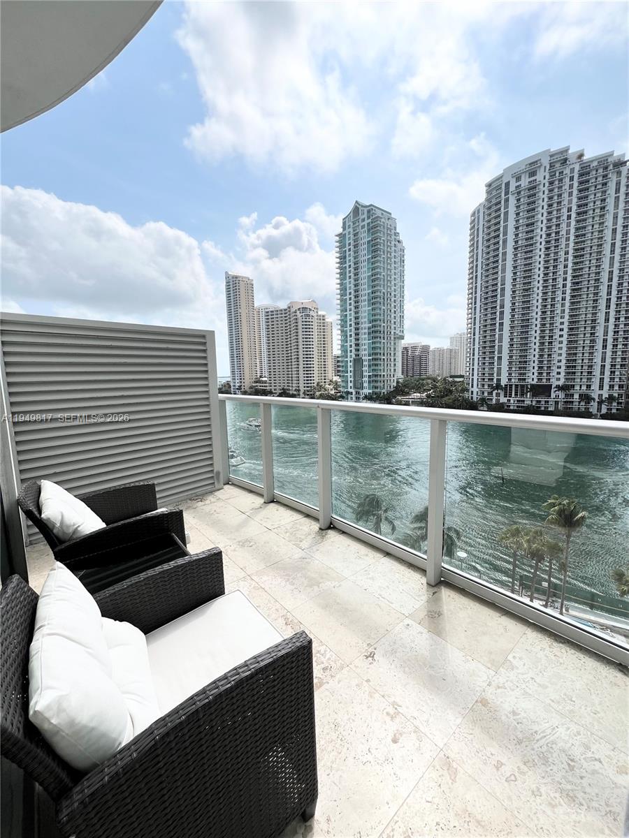 A balcony with two wicker chairs overlooks a body of water and city skyscrapers — 300 S Biscayne Blvd # 814, Miami FL 33131, MIAMI, FL