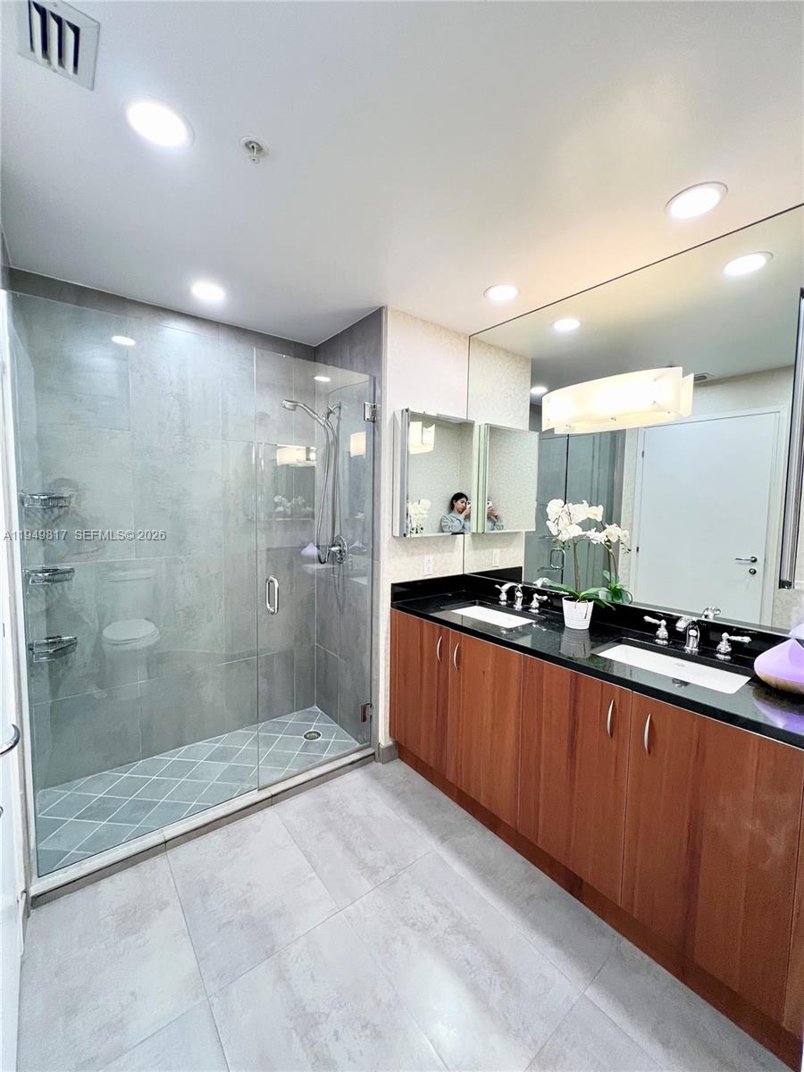 A bathroom features a glass-enclosed shower, a double vanity with wood cabinets, and large mirrors — 300 S Biscayne Blvd # 814, Miami FL 33131, MIAMI, FL