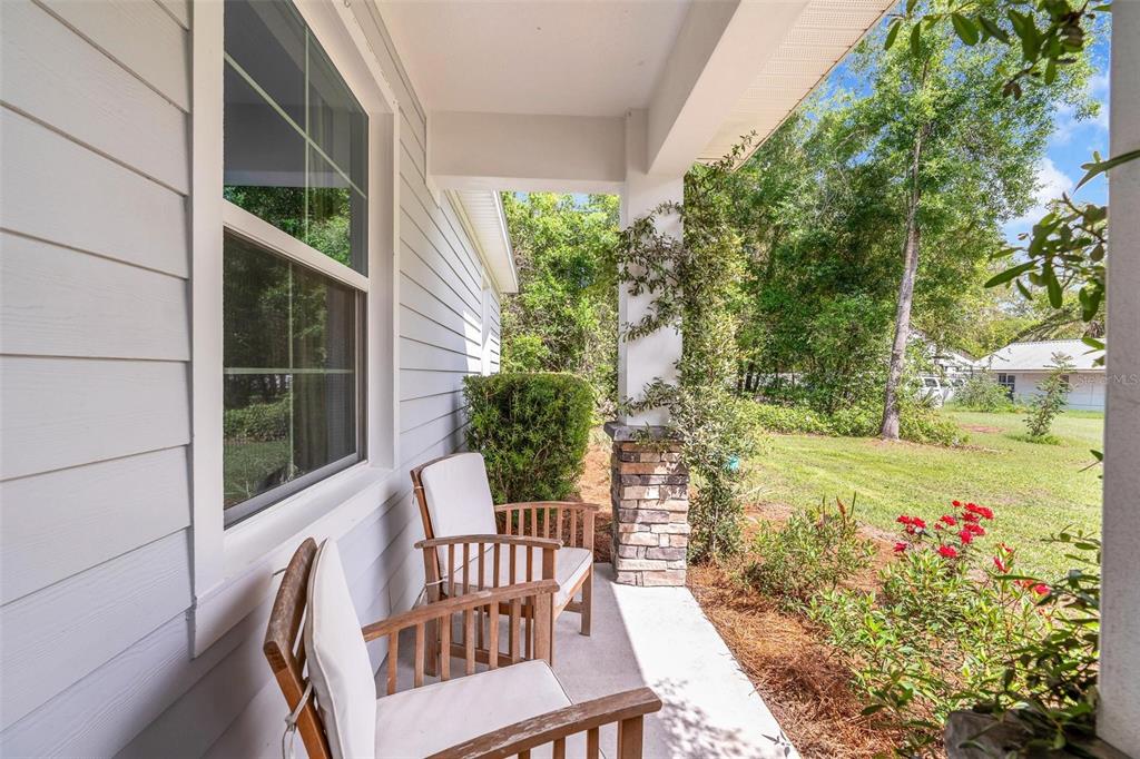 A covered front porch features two wooden chairs, a stone pillar, and a grassy yard — 1755 15TH STREET, ORANGE CITY, FL