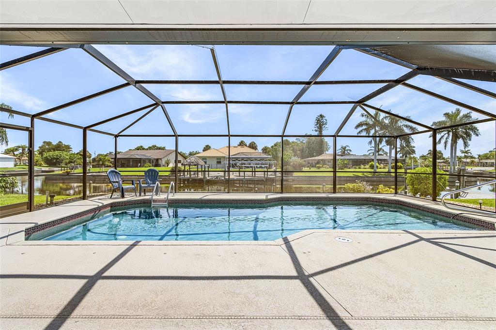 A screened-in swimming pool overlooks a canal with a dock and neighboring houses — 4504 SE 6TH PLACE UNIT A+B, CAPE CORAL, FL
