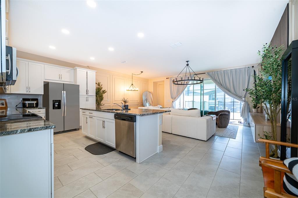 A kitchen with white cabinets and a granite island opens into a living room area — 1660 TROPICAL PALMS CIRCLE, KISSIMMEE, FL